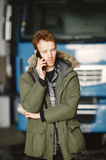 Мужчина разговаривает по телефону на фоне большого синего грузовика.